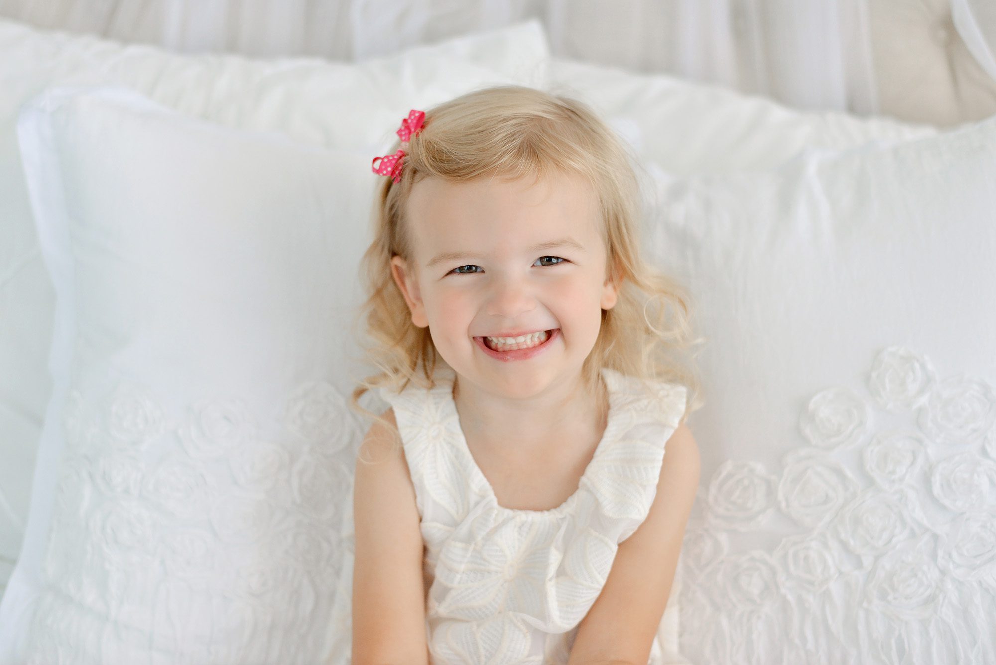 Mom and daughter happily snuggling and giggling on a white bed in a studio for a portrait session
