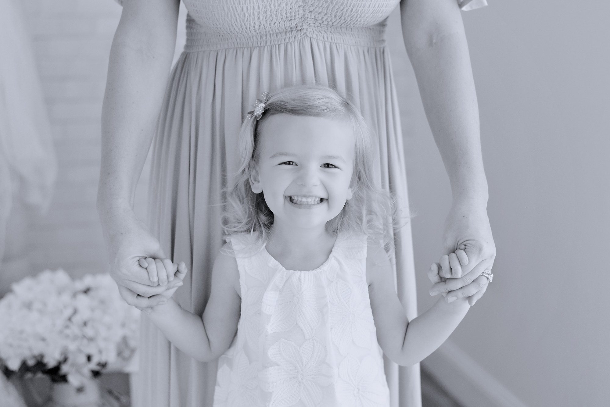 Mom and daughter happily snuggling and giggling on a white bed in a studio for a portrait session