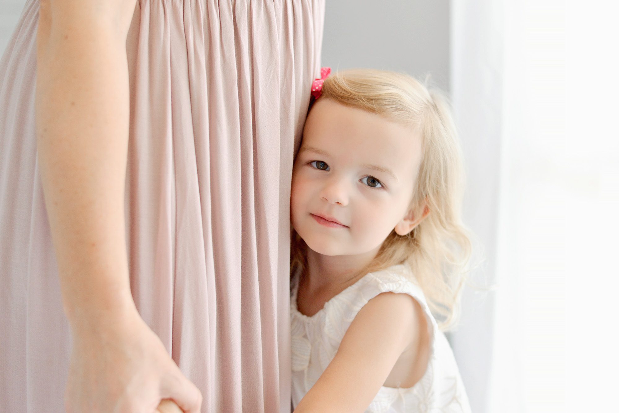 Mom and daughter happily snuggling and giggling on a white bed in a studio for a portrait session