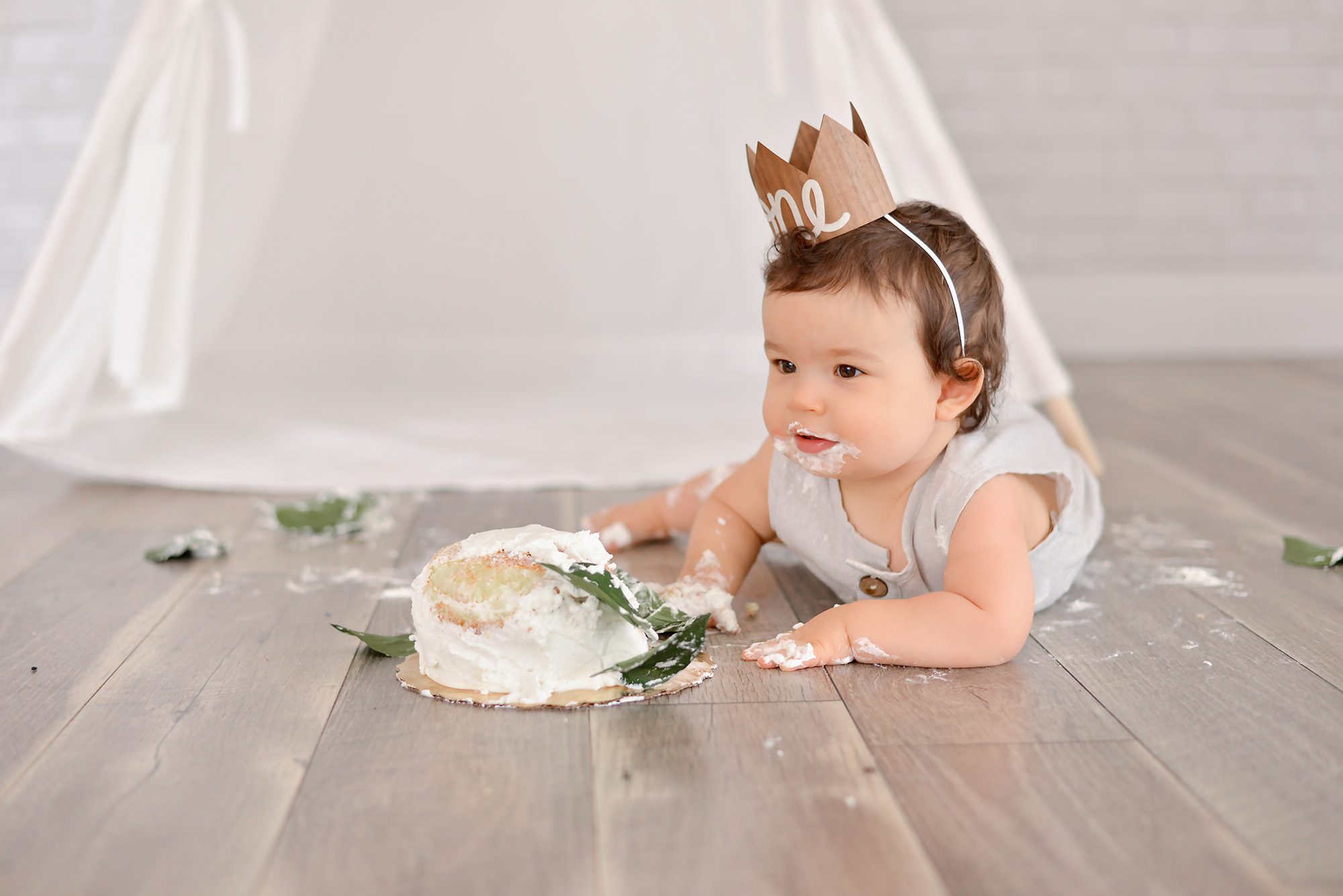 One year old baby boy with dark curls smashes white cake for his first birthday