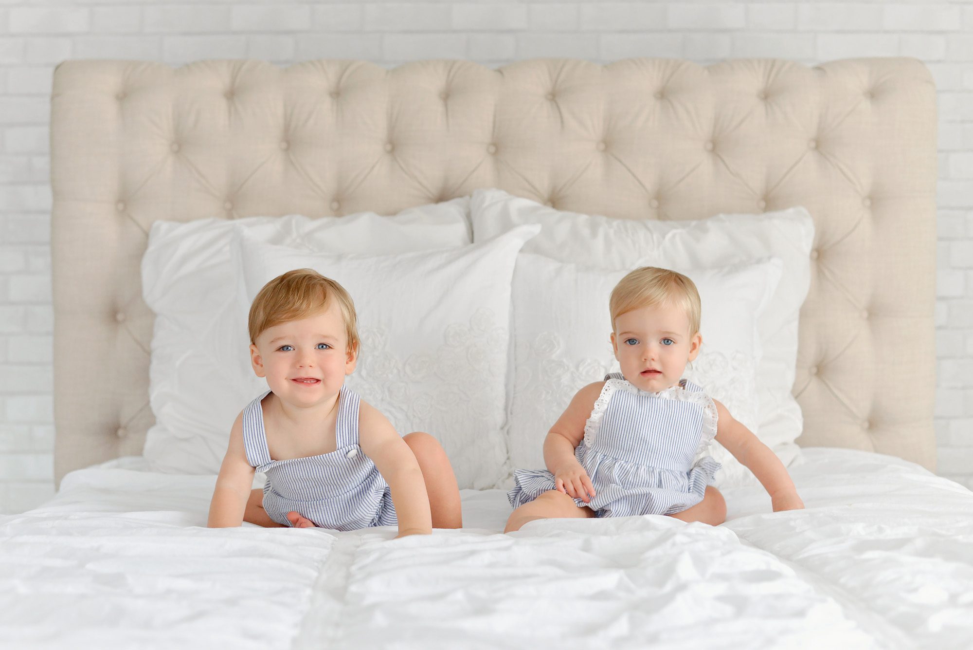 A set of blond haired blue eyed twins, one boy and one girl are being photographed in a white studio for their 1st birthday, which includes portraits and a cake smash at the end.