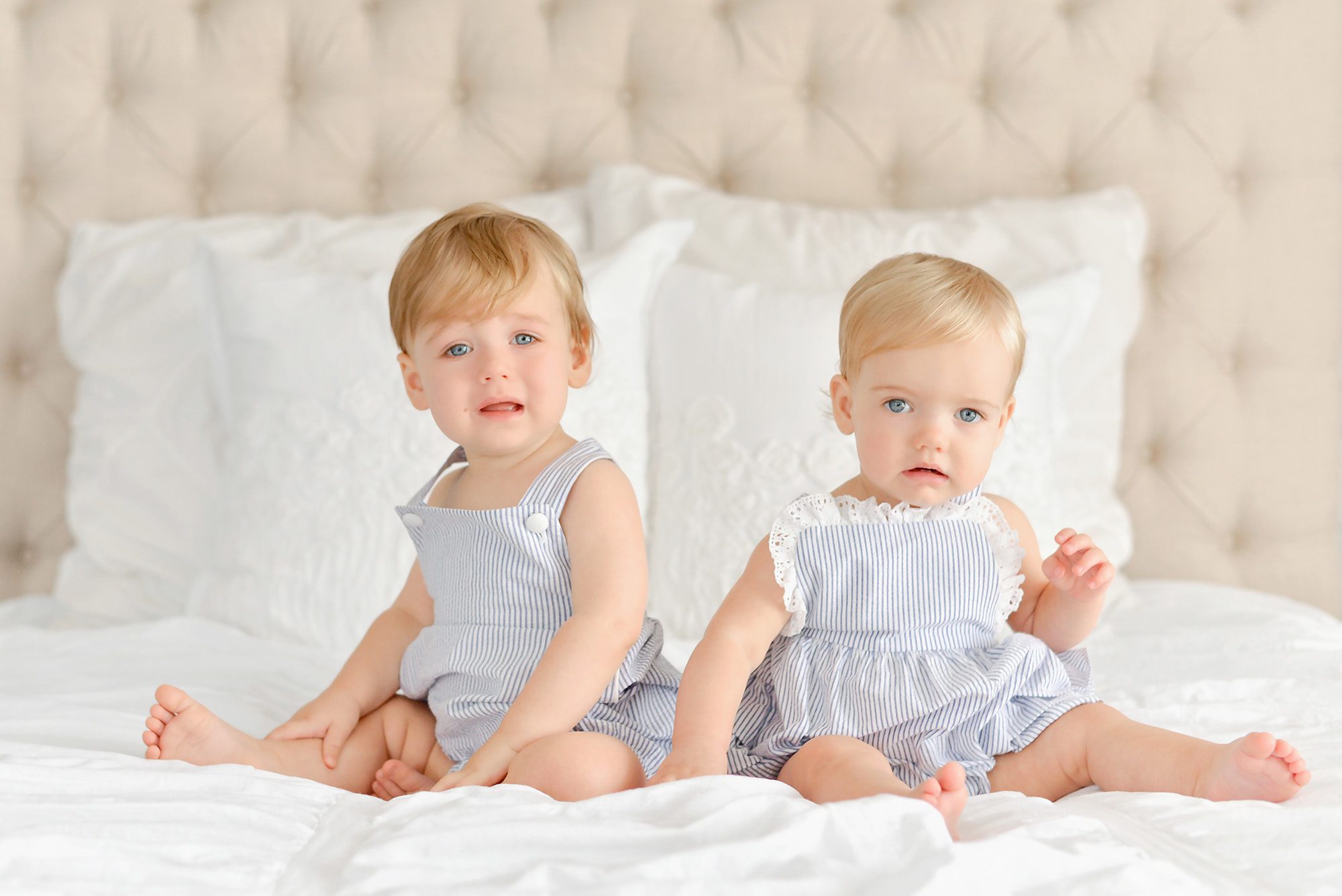 A set of blond haired blue eyed twins, one boy and one girl are being photographed in a white studio for their 1st birthday, which includes portraits and a cake smash at the end.