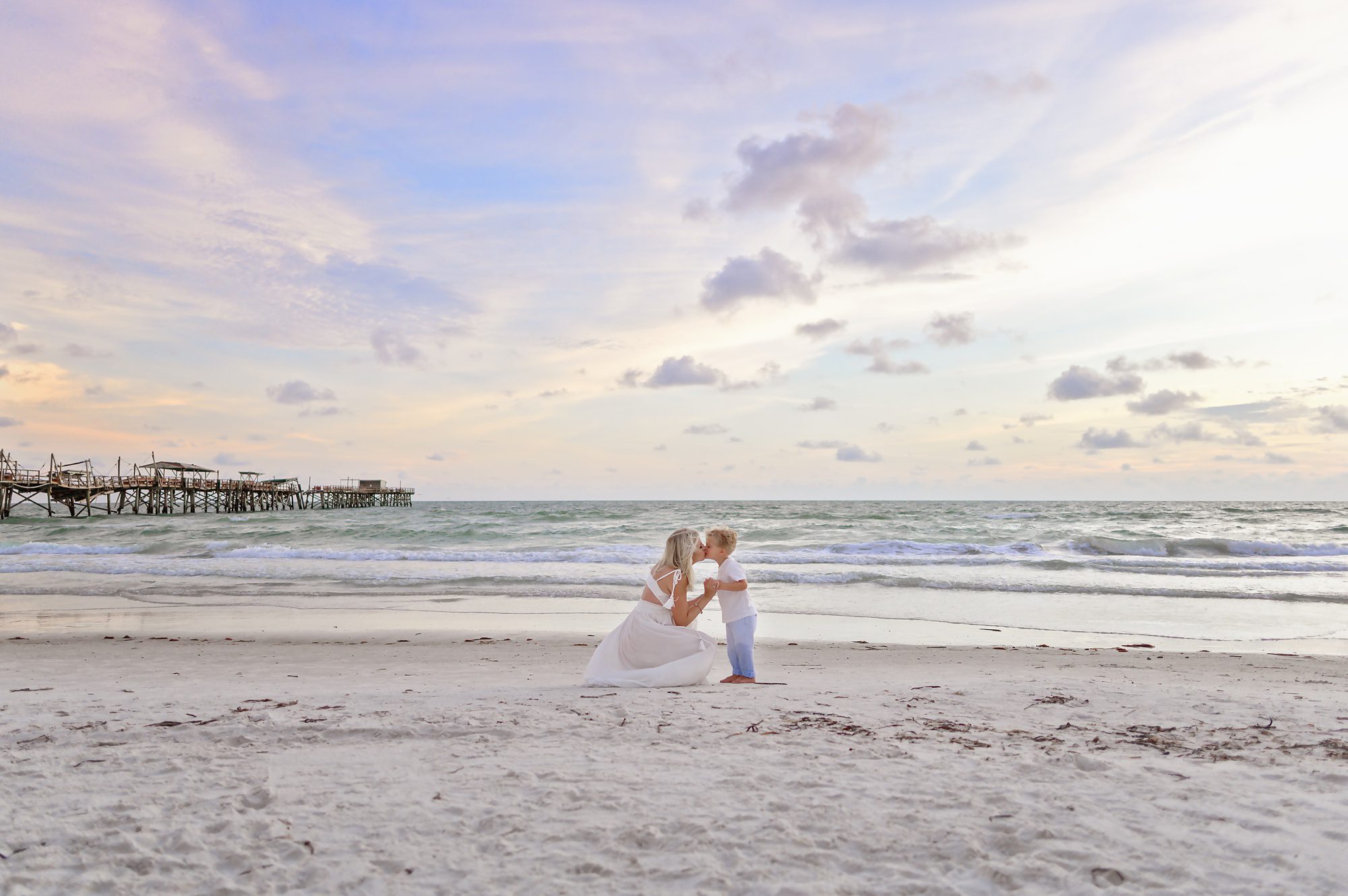 A beautiful blonde family of 3 gets family & maternity photos done on a beach in Redington Shores, FL at sunset time.
