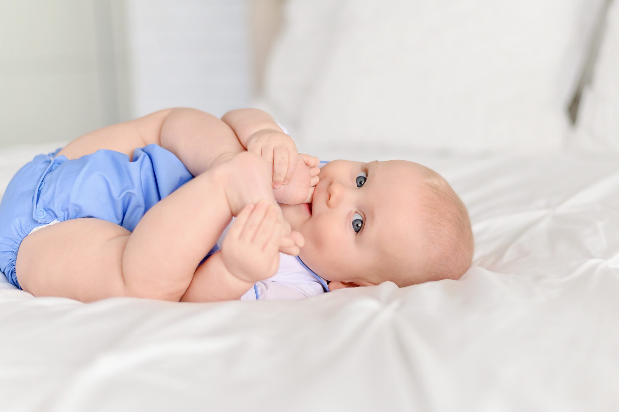 Fair skinned, blonde haired 6 month old baby boy gets his portrait taken on a white bed in a photography studio in Tampa, Florida.
