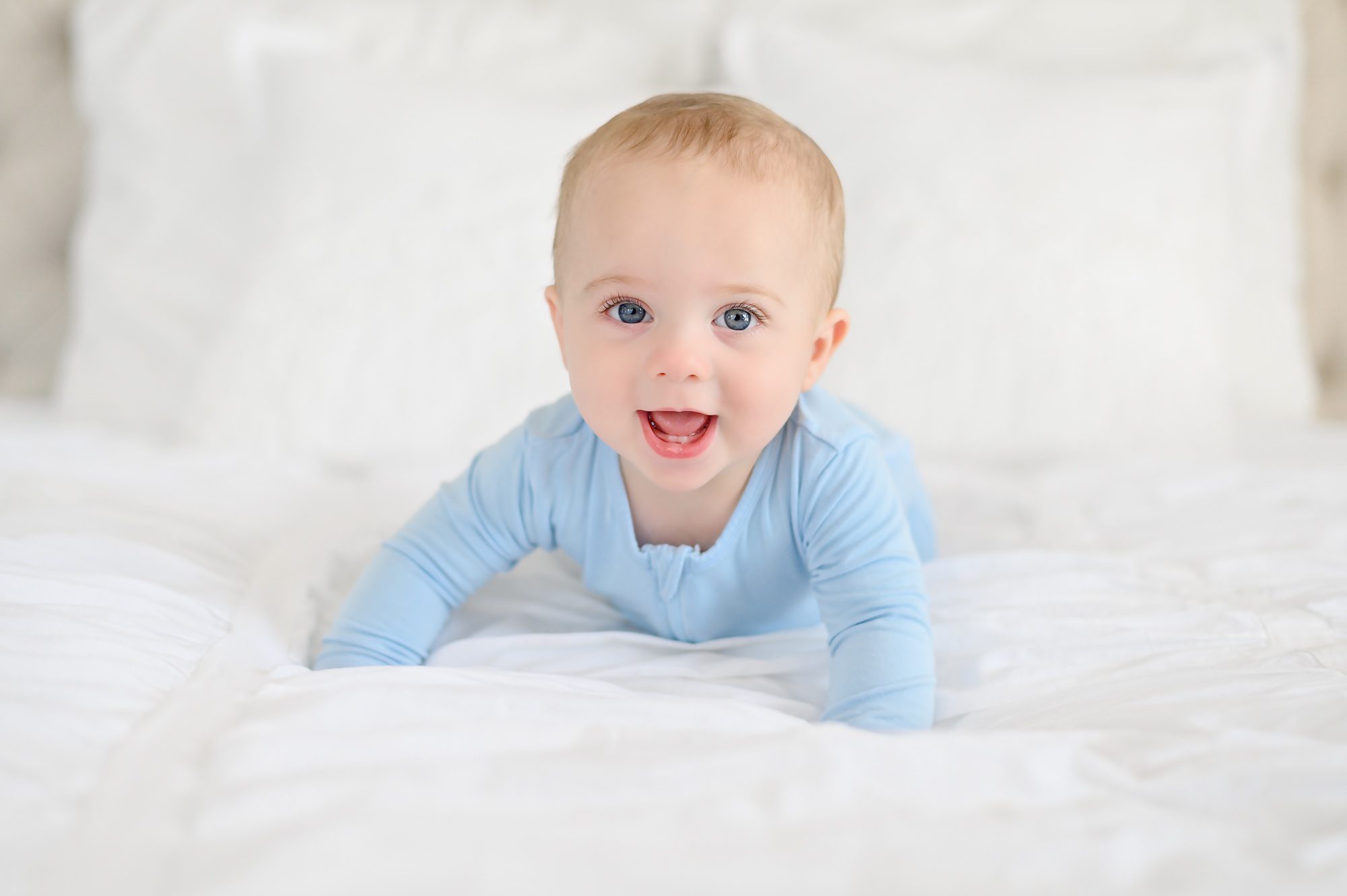 An adorable blue eyed baby boy gets his 6 month portraits done on a white bed in a studio in Tampa, FL and his older brother jumps in for a few.