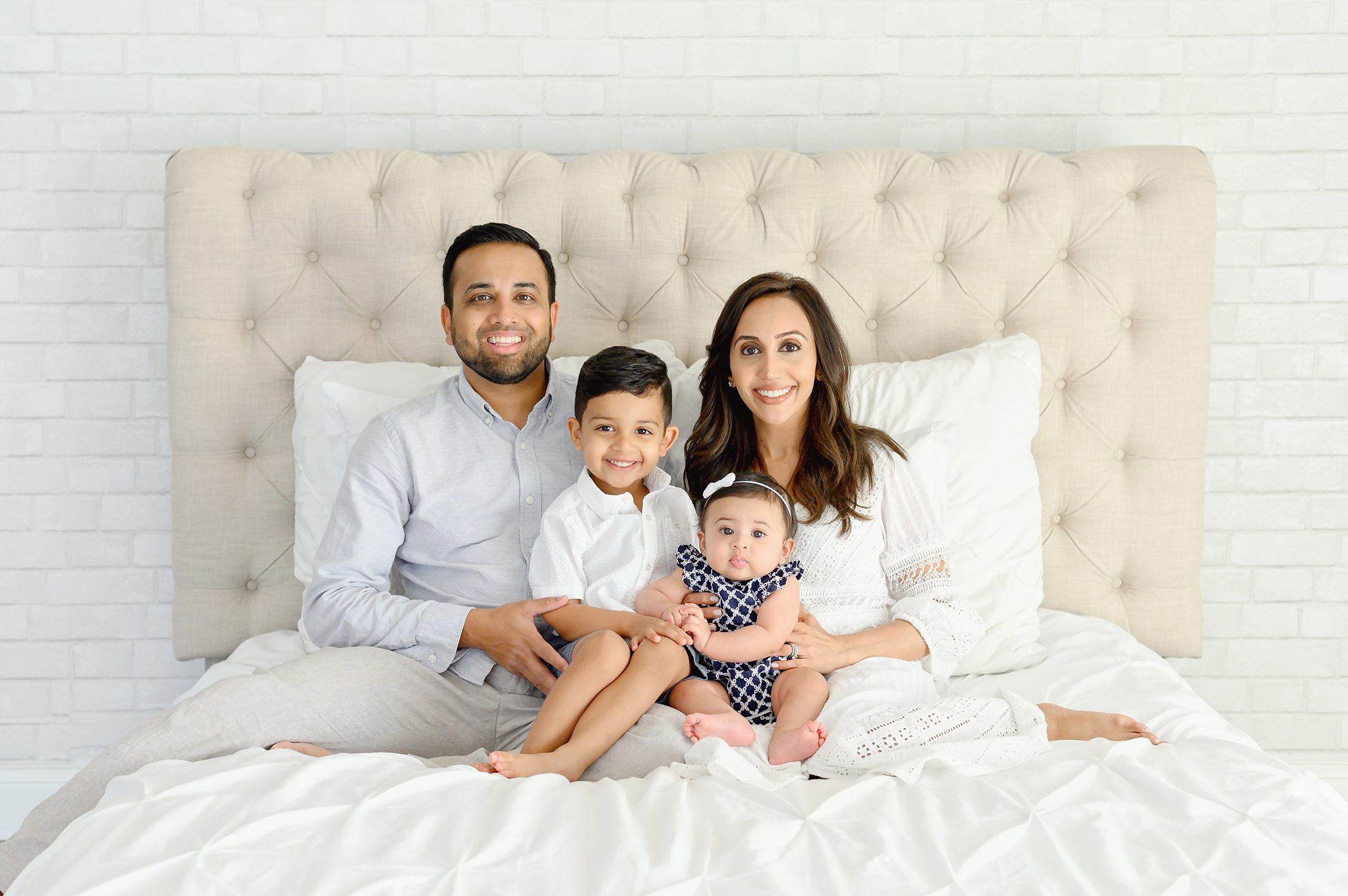 A family of 4 with a toddler boy and baby girl getting portraits done in a bright white studio.