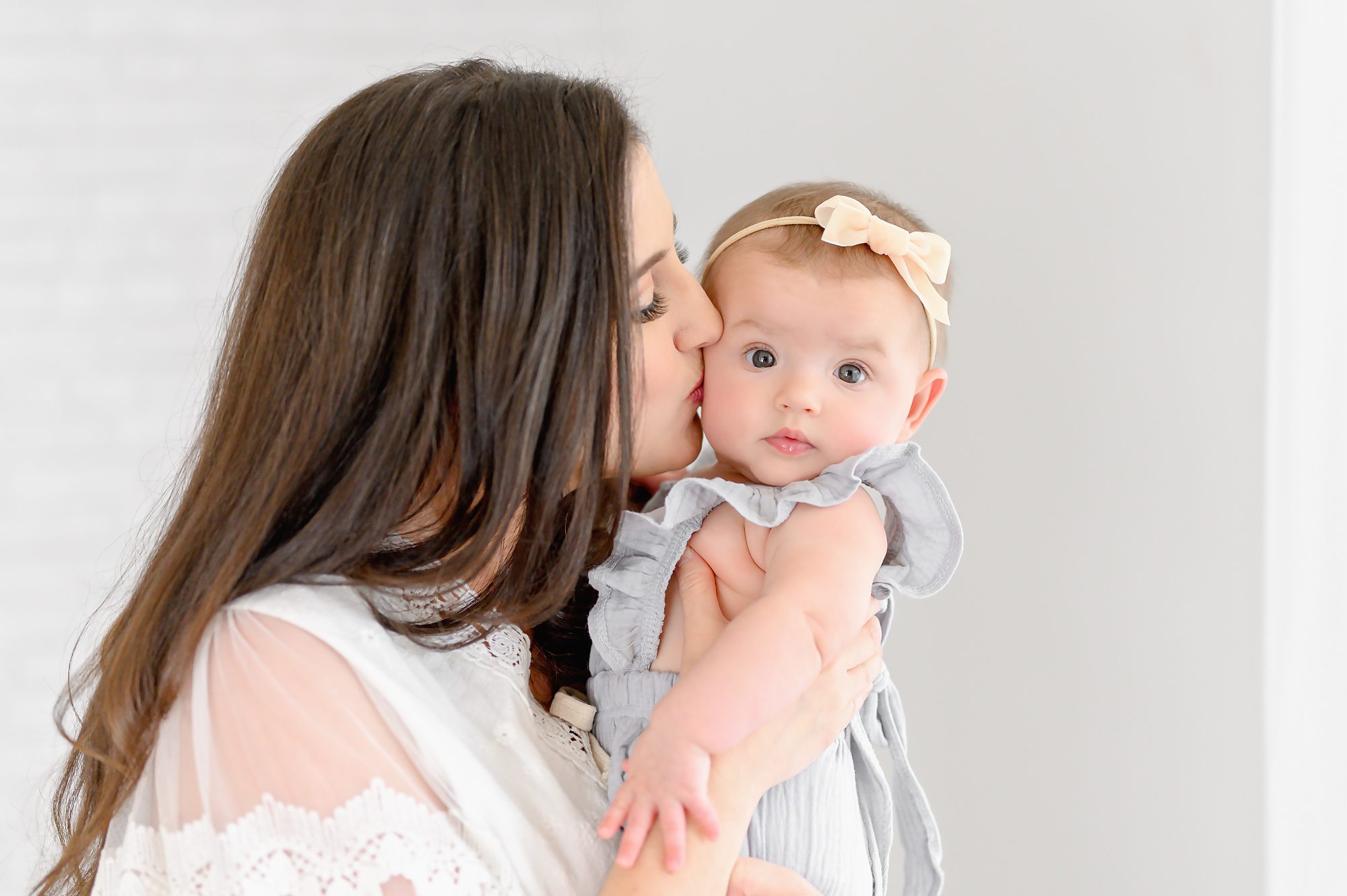 A young brunette mom and her six month old baby girl get mommy and me photos in a bright white studio in Tampa, Florida. 