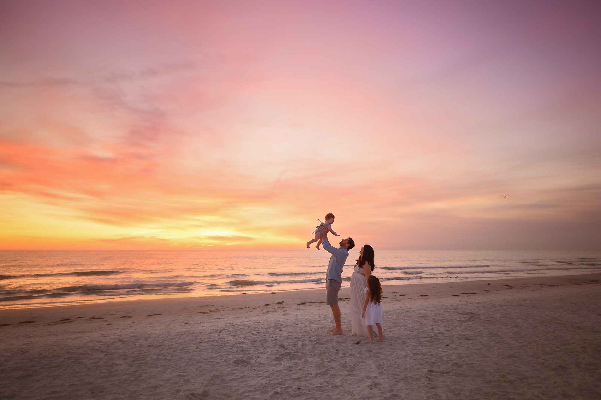 Family of four gets beach maternity portraits at sunset to celebrate their 3rd child on the way. 