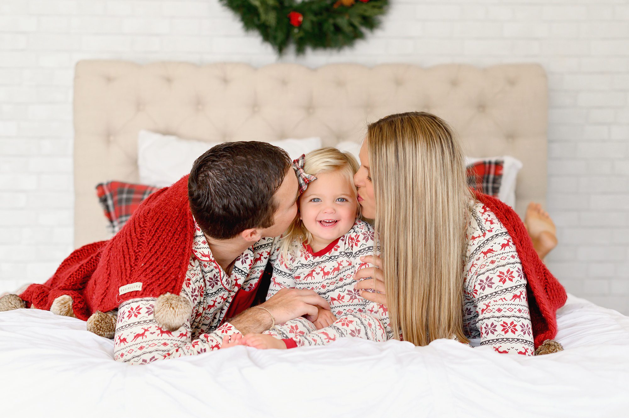 Children get Christmas themed pajama photos done on a bed in a white studio in Denver, Colorado. 