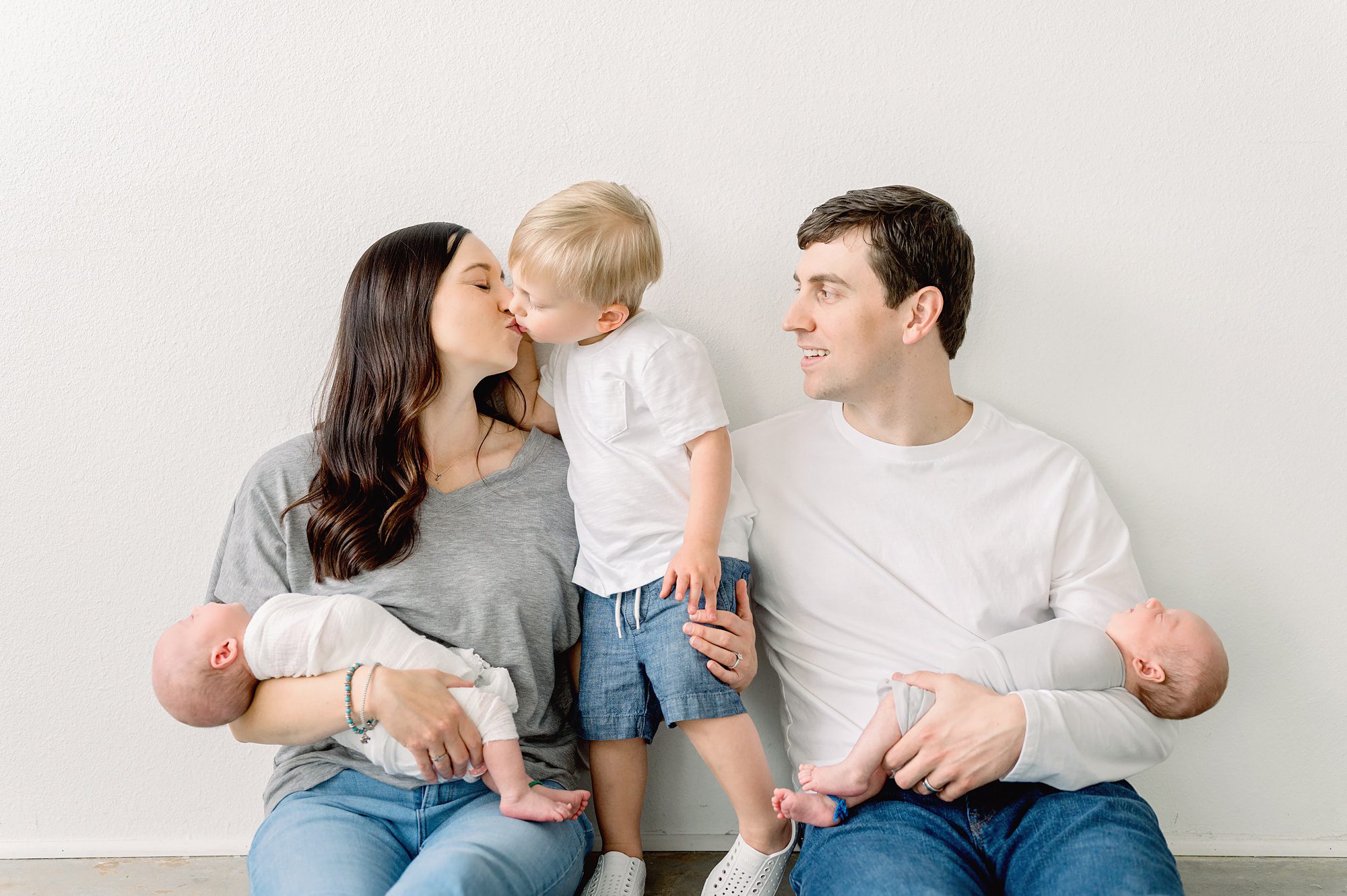 A family of five with newborn twin boys gets family photos done in a bright white studio in Denver Colorado with their older son.
